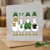 Square greeting card mockup featuring four geese dressed as leprechauns with beards, beer mugs, and a pot of gold.