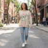 A woman walking in a city street wearing a sand-colored oversized sweatshirt with a retro checkered shamrock and pink bow design.