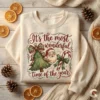 Cream-colored holiday sweatshirt mockup featuring a vintage watercolor Santa and Christmas tree design surrounded by dried oranges and pinecones.