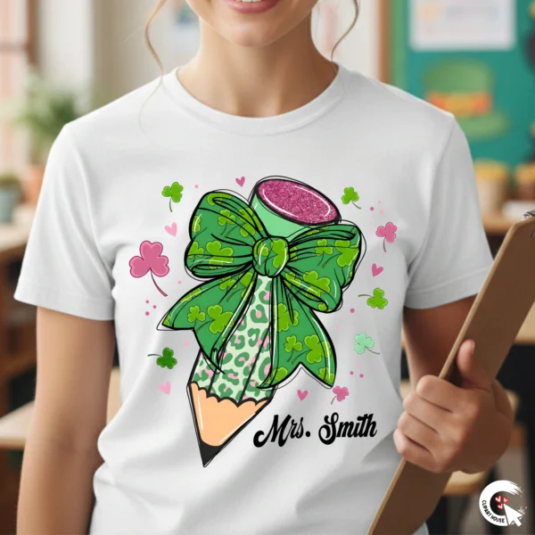Smiling female teacher standing in a classroom holding a clipboard, wearing a white t-shirt with a custom personalized One Lucky Teacher pencil design.