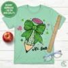 Flat lay of heather mint green t-shirt featuring leopard print shamrock teacher pencil design with personalized name Mrs. Smith, styled with red apple and ruler for teacher appreciation.