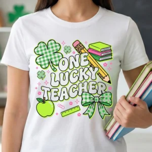 Retro coquette St Patrick's Day teacher t-shirt mockup featuring "One Lucky Teacher" design with green gingham shamrock, bow, pencil, and books on white shirt worn by female teacher holding colorful binders