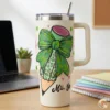 40oz cream stainless steel tumbler with handle featuring a wrap-around leopard print shamrock pencil design, sitting on a teacher's desk with a laptop.