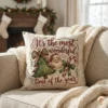 Decorative Christmas throw pillow on a sofa featuring a hand-painted watercolor Santa illustration in a cozy living room setting with a fireplace.