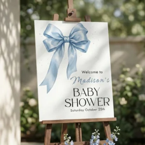 Watercolor blue bow baby shower welcome sign displayed on wooden easel with white flowers, coquette boy aesthetic.