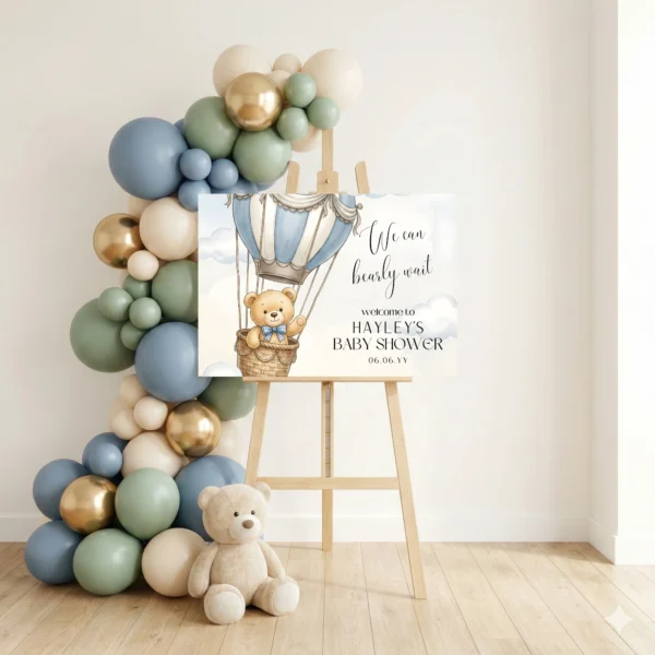 Large baby shower welcome sign displayed on easel surrounded by luxury blue and gold balloon arch decoration.