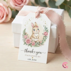Coquette watercolor bunny 1st birthday favor tag tied with a pink ribbon to a white square gift box.