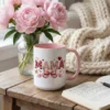 15oz white and pink ceramic coffee mug featuring the Coquette Mama faux texture design, styled on a wooden table with pink peonies.