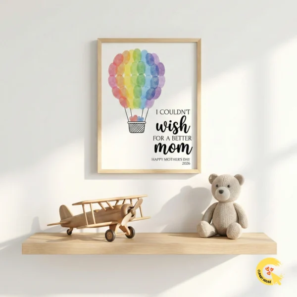 A light wood frame hanging on a white nursery wall showing the rainbow fingerprint hot air balloon art. A wooden toy plane and teddy bear sit on the shelf below.