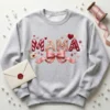 Light heather grey sweatshirt displaying a 3D latch hook yarn Mama Valentine design, styled with a wax seal envelope.