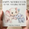 Close up of two hands holding a freshly printed square Mother's Day card, showing the crisp watercolor elephant illustration on textured cardstock.
